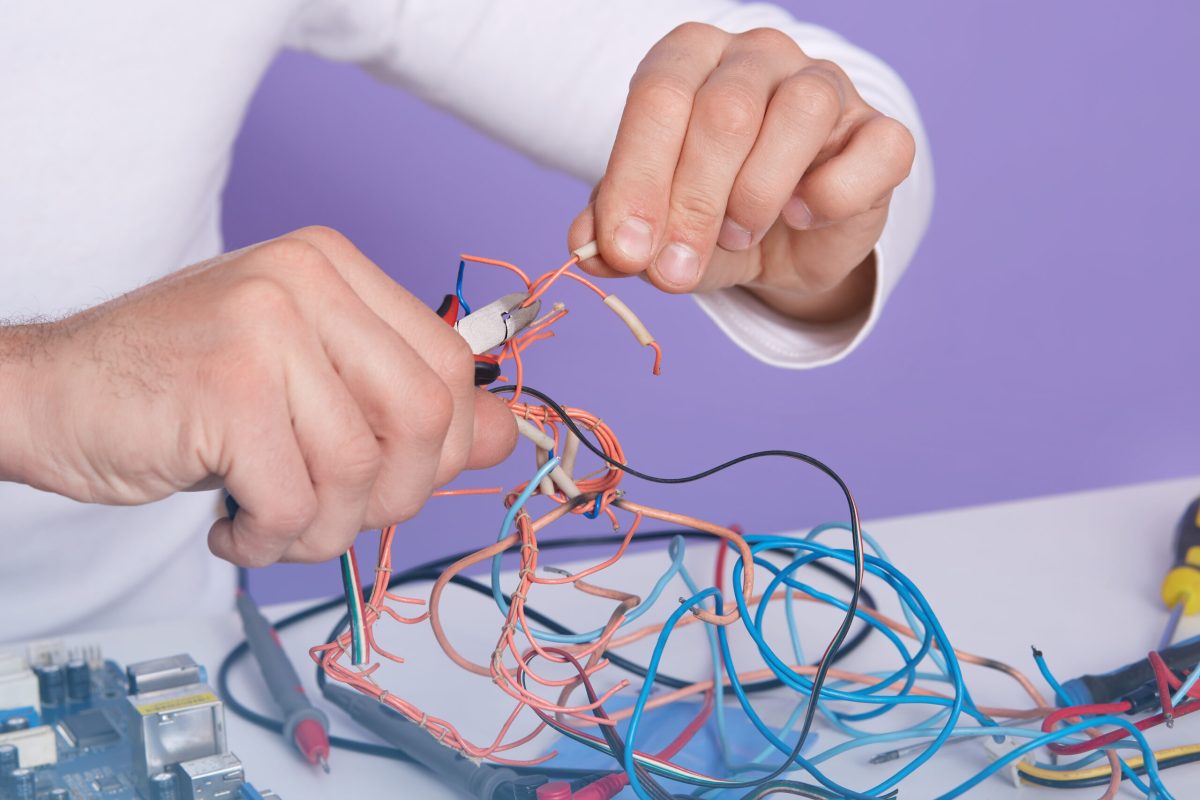 Closeup indoor picture of man hands holding side cutting pillers and conductors, doing his work in proper way, making repair by himself, sitting at special lab. Electronic engineering concept.