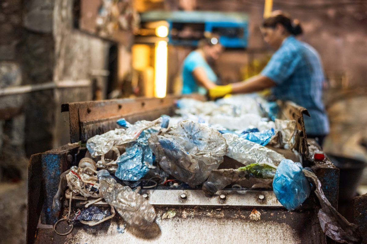 Plastic garbage on a conveyor belt at waste recycling factory. Workers on the background