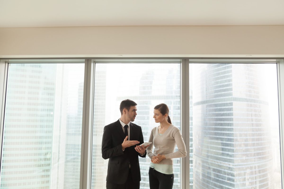 Smiling colleagues discussing business project with tablet in office, happy businessman and businesswoman talking about digital apps for easy daily management, employees communicating near big window